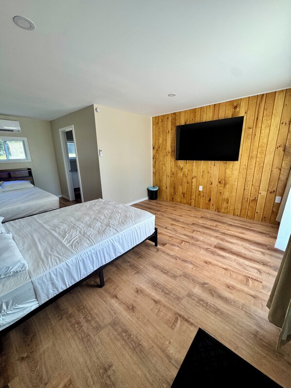 Een slaapkamer met twee bedden, houten vloeren, een wandtelevisie en een raam.