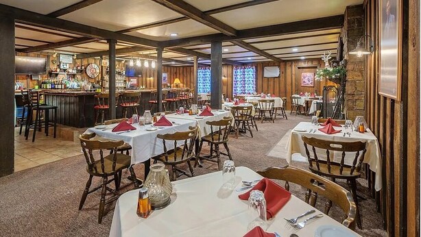 A restaurant with multiple tables and chairs, a bar area in the background, and a rustic interior design. - Cascade Inn (Lake Placid)