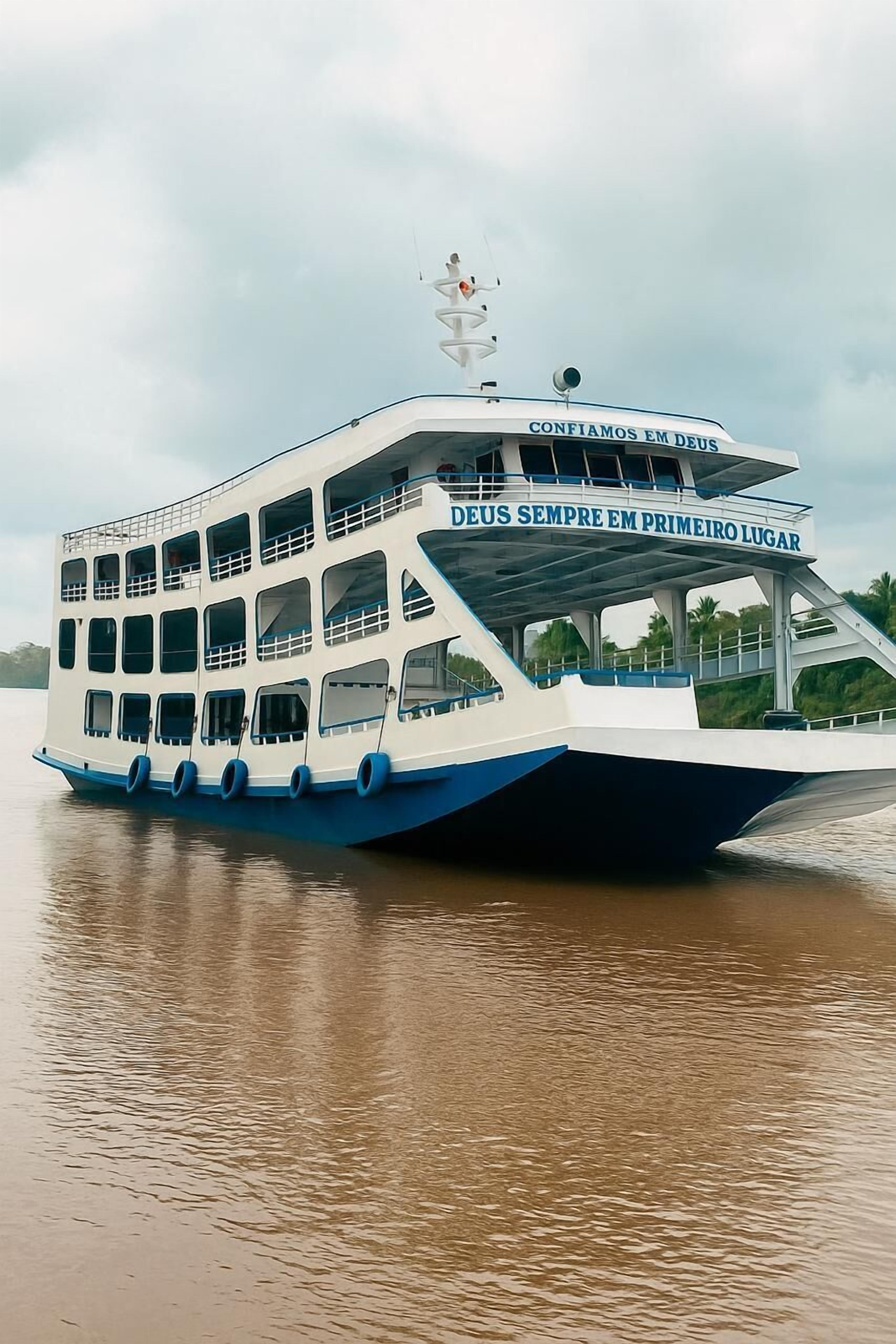 A multi-deck boat with text reading "Deus sempre em primeiro lugar" and "Confio em Deus" on the upper deck.