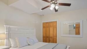 A bedroom with a bed, nightstand, wooden wardrobe, ceiling fan, and a mirror on the wall.