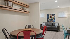 A modern living room with a round dining table, red chairs, a grey sofa, and a painting on the wall.