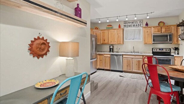 A modern kitchen with wooden cabinets, stainless steel appliances, and a dining area with a table and chairs.