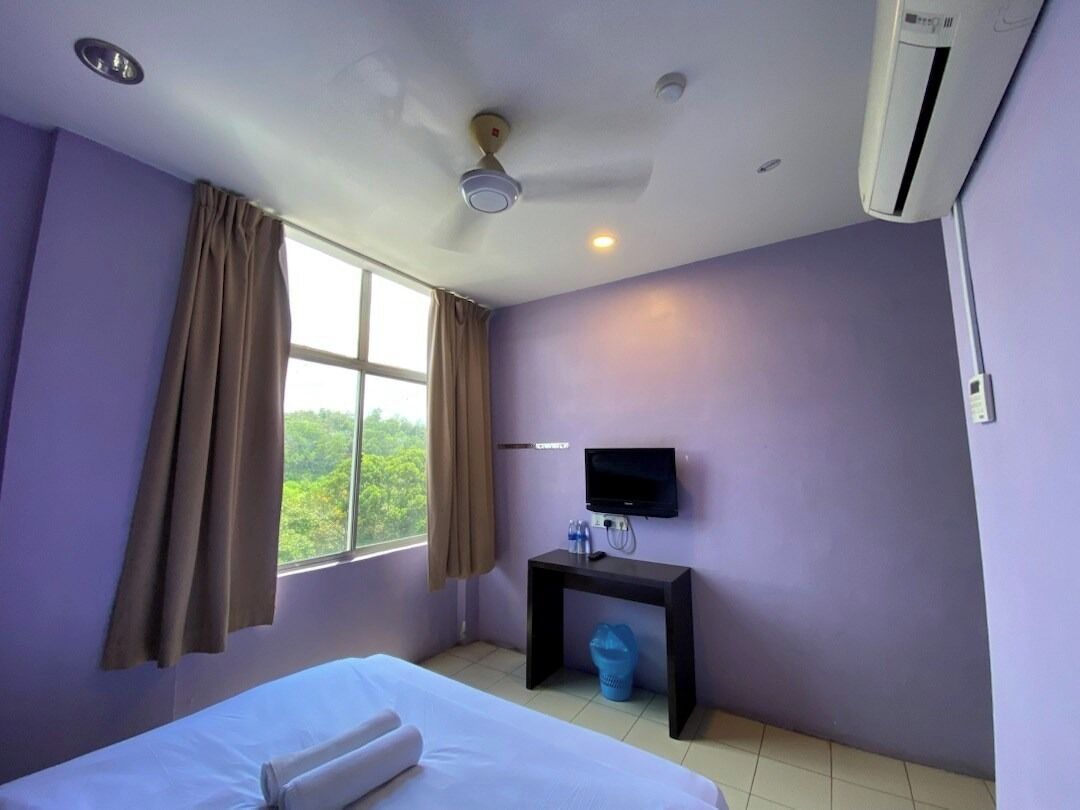Habitación de hotel con cama, televisión sobre un mueble, ventilador de techo y ventana con cortinas.