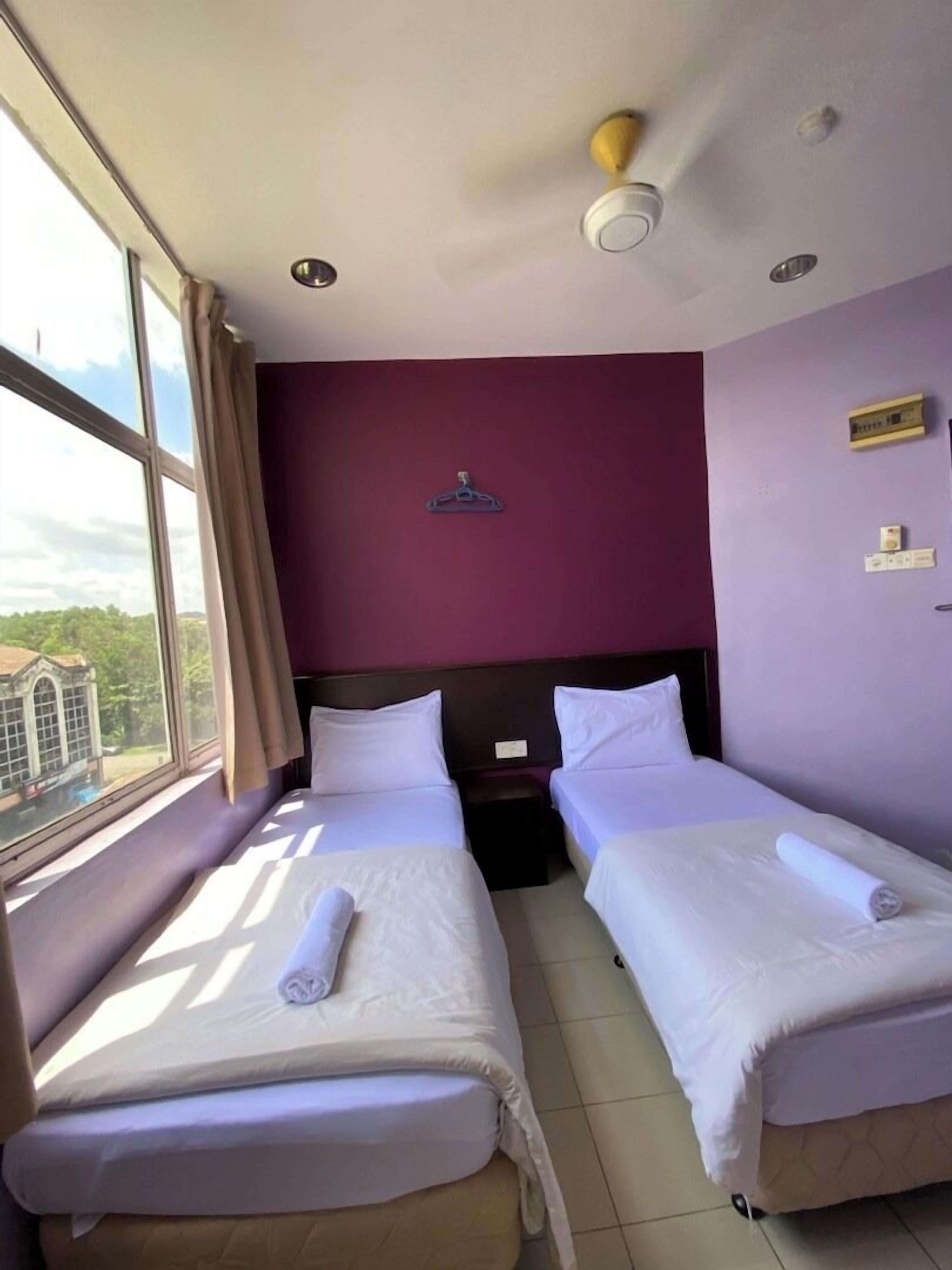 A hotel room with two beds, a large window, and a view of a building outside.