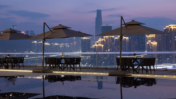An outdoor dining area with tables and umbrellas, overlooking a city skyline and a bridge. - Wanda Moments Chongqing Liziba (Chongqing)