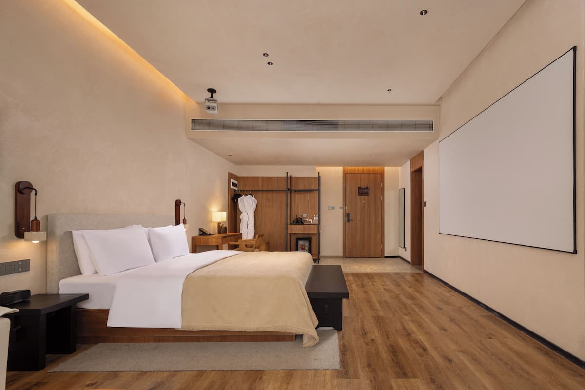 A modern hotel room with a large bed, bedside tables, a desk, a robe, and a wardrobe.