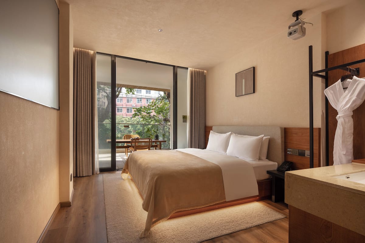 A hotel room with a bed, a desk, a chair, a bathroom, and a view of buildings outside.