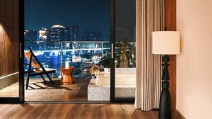 Een moderne kamer met uitzicht over de stad, een stoel, een klein tafeltje en een lamp.