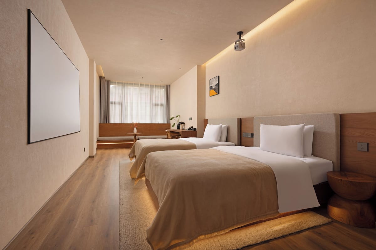 A hotel room with two beds, a large window with curtains, a flat-screen TV, and a wooden floor.