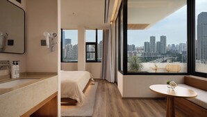 A modern hotel room with a large window, a bed, a bathroom with a vanity, and a small table with a vase. - Wanda Moments Chongqing Liziba (Chongqing)