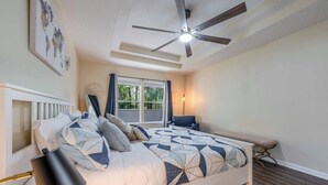 A bedroom with a bed, a ceiling fan, a bedside table, a chair, and a window.