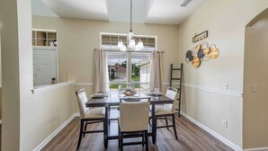 A dining area with a table set for four, a chandelier, and a decorative wall piece.