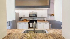 A modern kitchen with white cabinets, a stainless steel sink, a granite countertop, a microwave, and a stove.