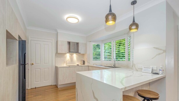 Een moderne keuken met een marmeren kookeiland, houten krukken en hanglampen.