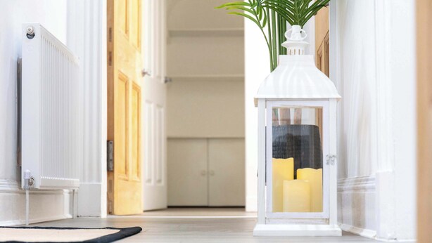 A hallway with a white radiator, a white lantern with candles, and a wooden door in the background.
