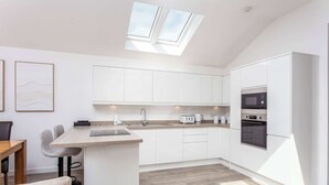 A modern kitchen with white cabinets, a built-in oven, and a skylight.