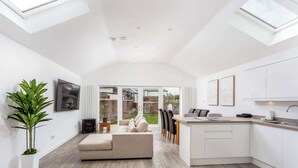 A modern kitchen with white cabinetry, a dining area with a sofa, and a large window overlooking a garden.