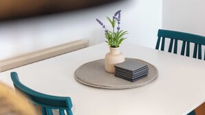 Taula blanca amb un vas beix contenint plantes de lavanda, una pila de llibres negres i una sovina teixida.