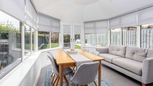 A modern living room with a wooden dining table, grey sofa, and large windows. - No15 Ellis House - Donnini Apartments (Kilmarnock)