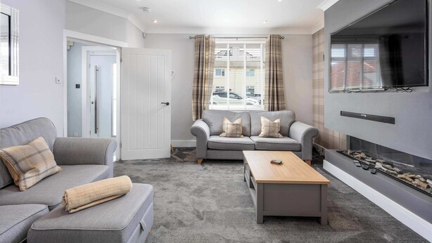 A modern living room with grey sofas, a wooden coffee table, and a fireplace. - No15 Ellis House - Donnini Apartments (Kilmarnock)