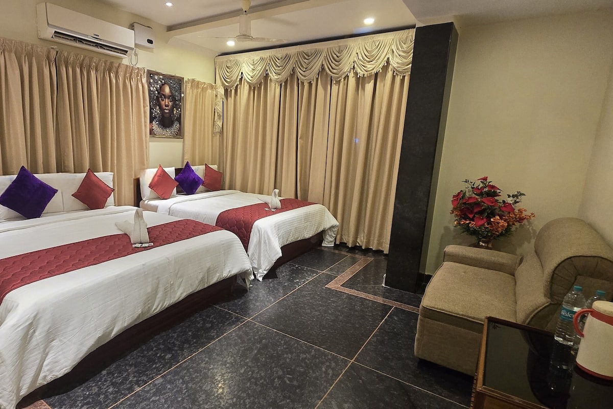 Quarto de hotel com duas camas, um frigorífico, uma mesa de centro e um vaso de flores.