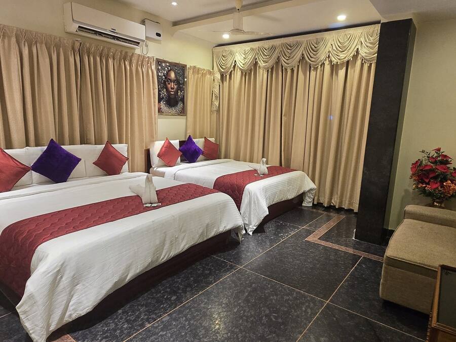 A hotel room with two beds, a refrigerator, a coffee table, and a flower vase.