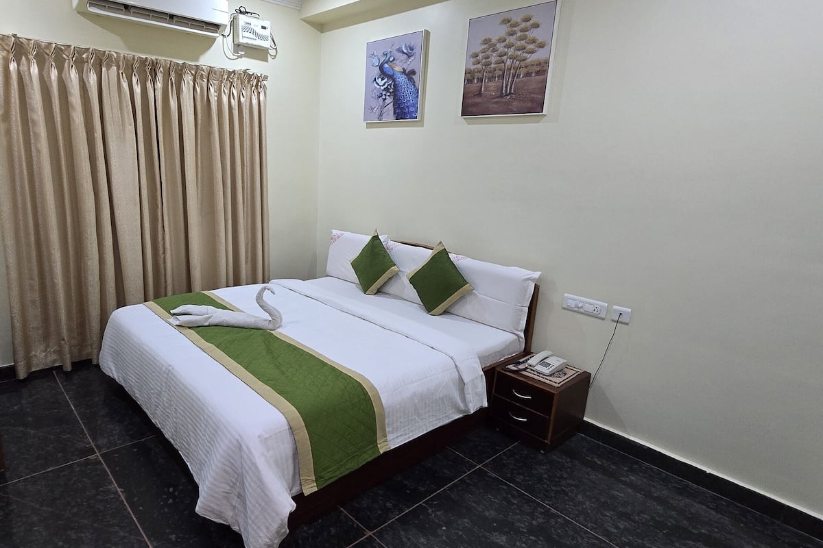 Quarto de hotel com uma cama, mesa de cabeceira, ar condicionado fixado na parede e duas imagens emolduradas.
