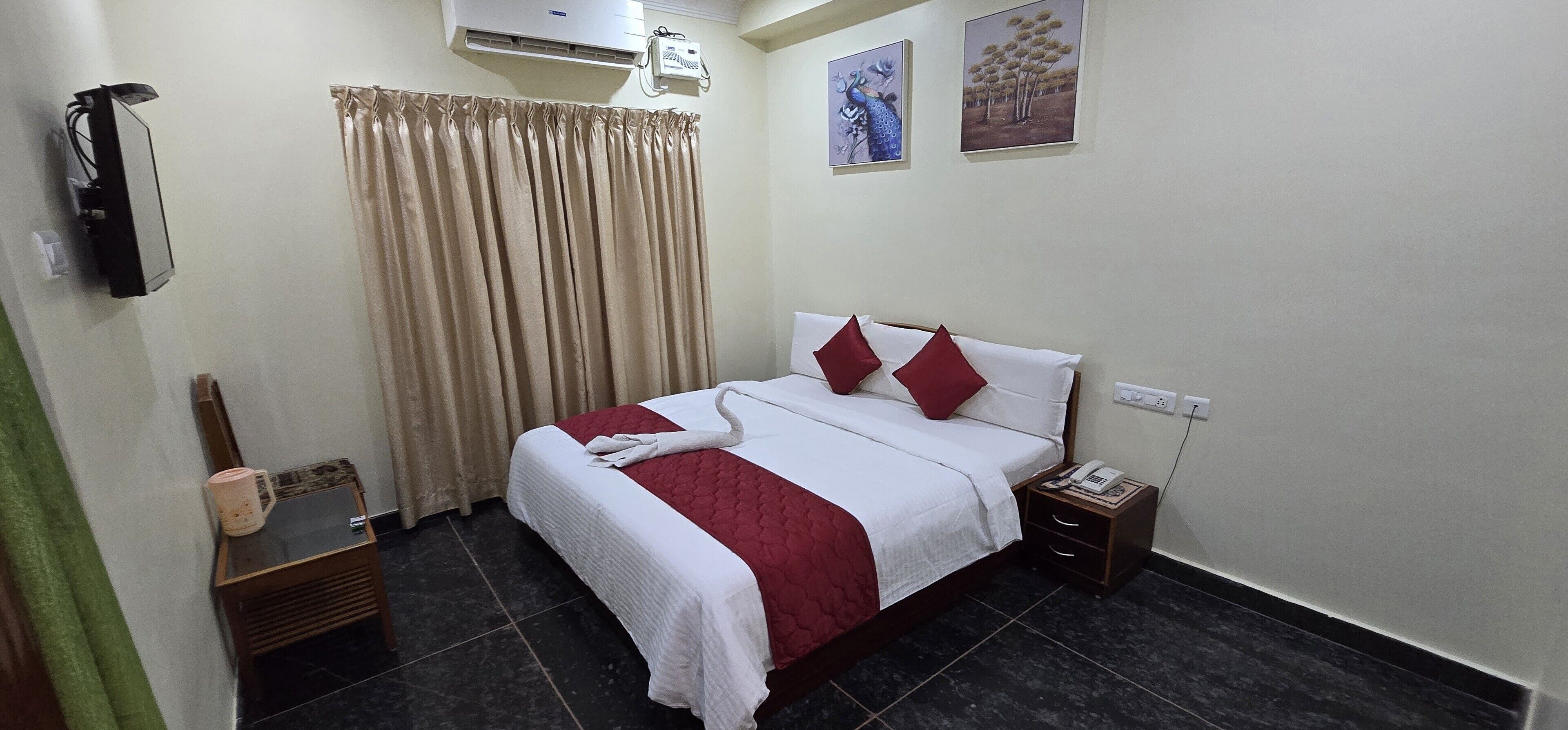 Habitación de hotel ordenada con cama, mesita de noche, teléfono y aire acondicionado instalado en la pared.