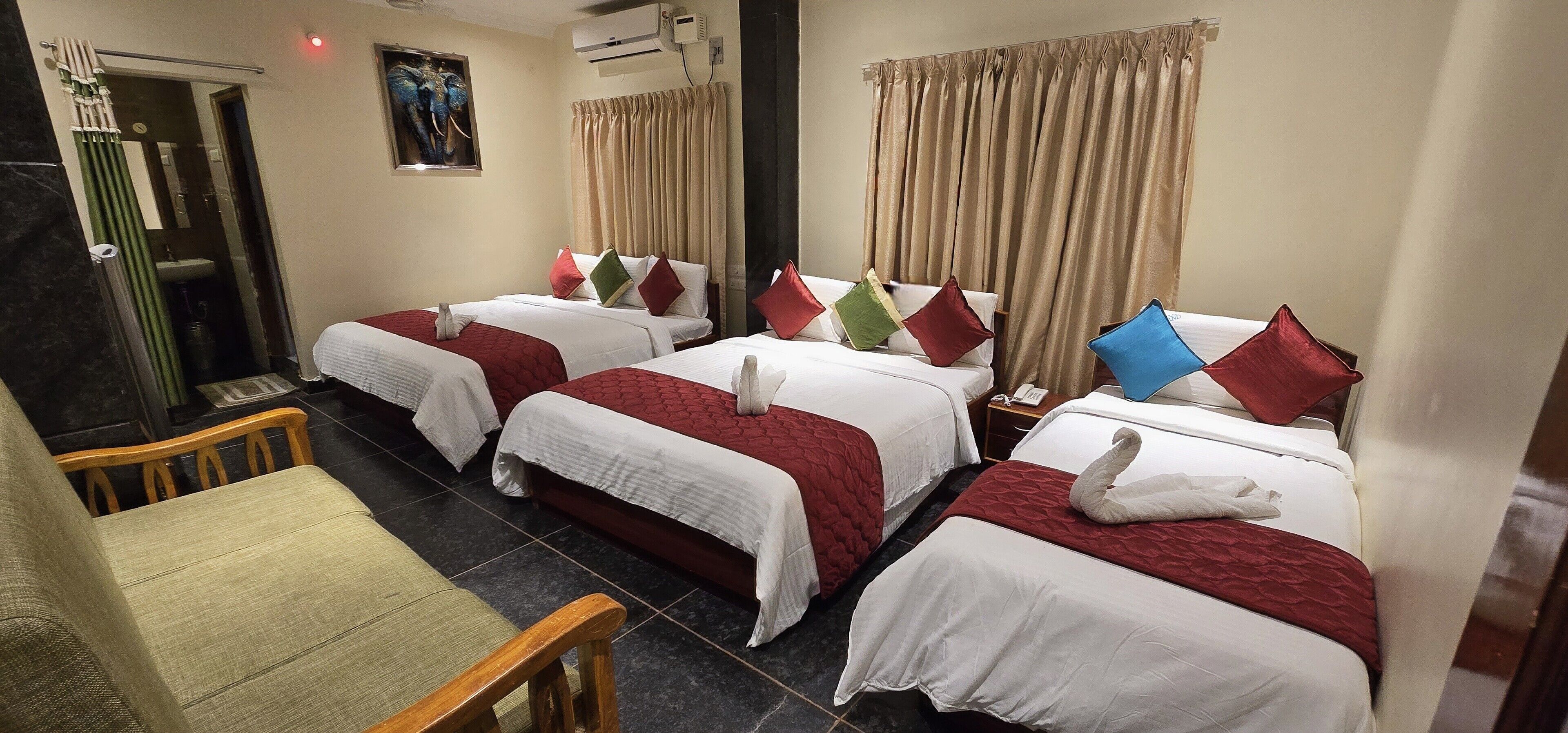 Quarto de hotel com três camas, cada uma com roupa de cama vermelha e branca, e uma cadeira.