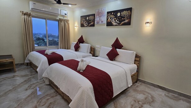 A hotel room with two beds, a nightstand, a window with curtains, and artwork on the walls. - HOTEL KSR GRAND (Srikalahasti)