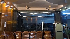 A lobby with wooden seating, a coffee machine, and a refrigerator. - HOTEL KSR GRAND (Srikalahasti)