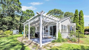 Un patio techado con una pérgola, una casita con porche y un patio cercado.