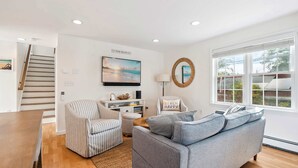 Ein Wohnzimmer mit grauem Sofa, Sesseln mit Streifenmuster und einem Bild von einer Strandlandschaft.