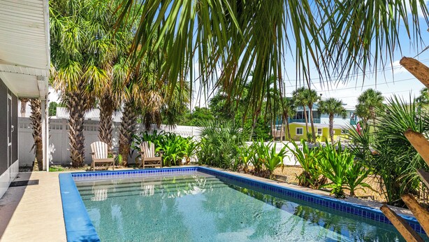 A clear swimming pool with a blue tiled edge, surrounded by palm trees and other greenery. - Island home in paradise (Siesta Key)
