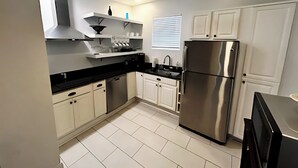 A modern kitchen with white cabinets, a stainless steel refrigerator, and a black countertop.