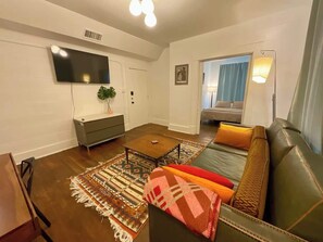 Una sala de estar con sofá, mesa de centro y televisor montado en la pared.
