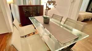 A dining area with a glass table, white chairs, a vase with flowers, a lamp, and a wooden cabinet.