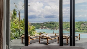 Un balcón con dos camas de mimbre, vista al mar y plantas tropicales.