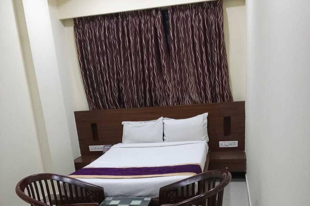 A hotel room with a bed, a small table with a chessboard, two wooden chairs, and a curtain with a wavy pattern.