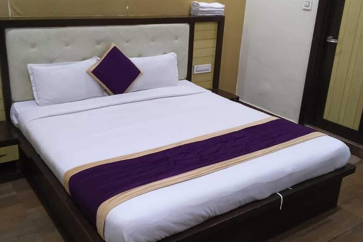 A neatly made bed with white bedding and a purple accent, a wooden headboard, and a wooden nightstand with a drawer.