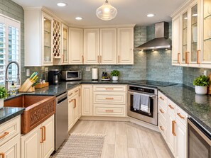 A modern kitchen with white cabinetry, a stainless steel range hood, and a granite countertop.