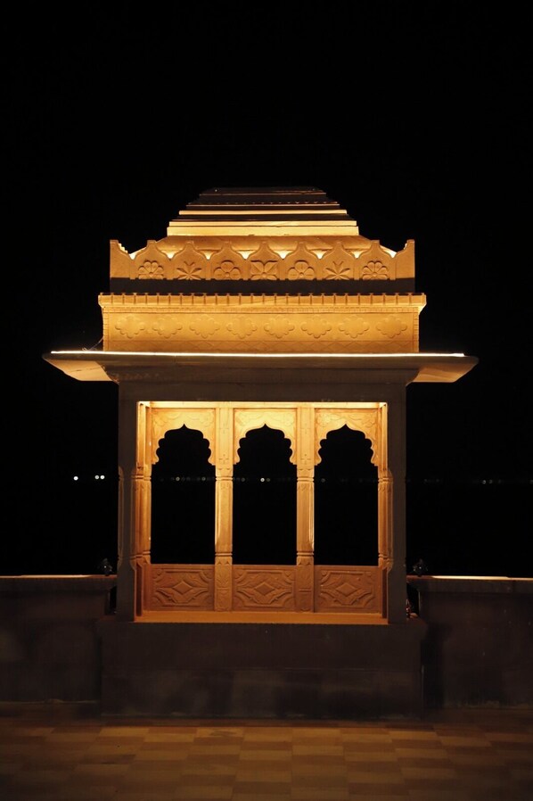 A night view of a traditional structure with ornate carvings and a tiered roof, illuminated by warm lighting.