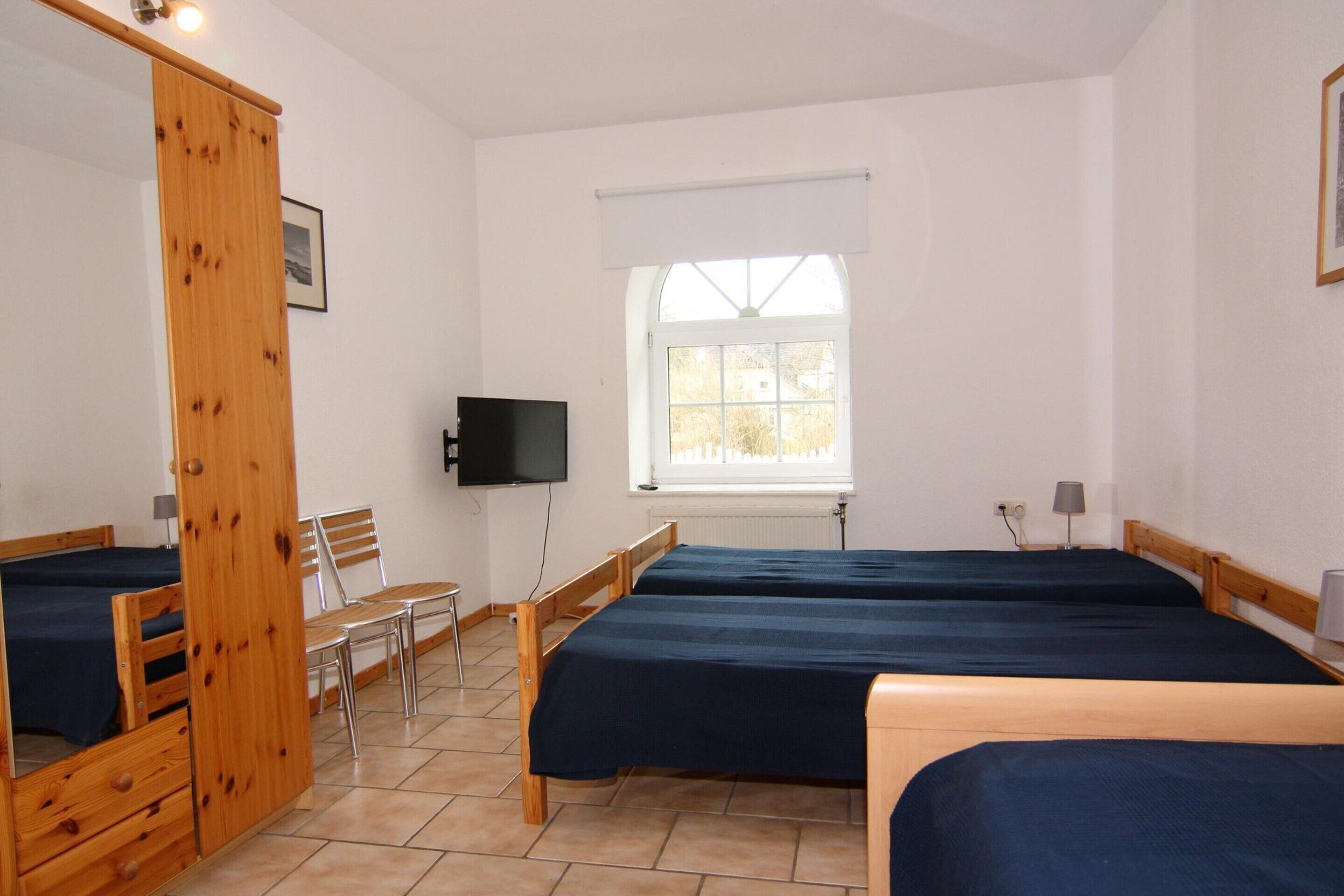A room with three wooden beds, a television, a window, and a chair.