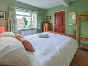 Ein ordentlich bezogenes Bett mit Kissen, ein Fenster mit Vorhängen, ein Holzschrank und ein Spiegel an der Wand.