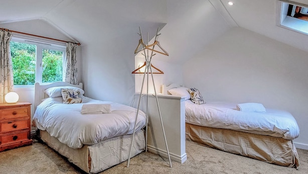 A bedroom with two beds, a bedside table, a lamp, and a window with curtains. - 4 bedroom accommodation in Thornton Watlass, near Masham (Thornton Watlass, near Masham)