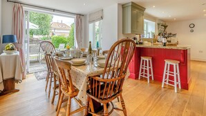 A dining area with wooden chairs, a table set for four, and a kitchen with red cabinets and a bar area.
