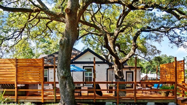 A wooden deck with a house in the background, surrounded by trees.