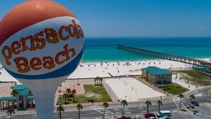 A beach scene with a large sign reading "Pensacola Beach" and a pier extending into the water.
