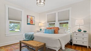 A bedroom with a bed, bedside tables, a bench, and a window with blinds.