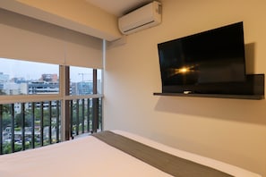 Habitación de hotel con un ventanal grande, un televisor de pantalla plana montado en la pared y una cama con cabecera.